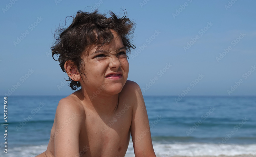 A young boy looks very unhappy at the idea of leaving the beach to go home A young boy looks very unhappy at the idea of leaving the beach to go home