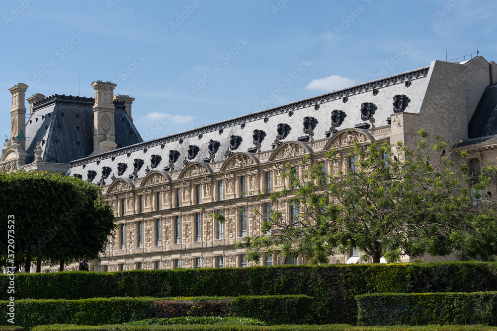 Close-up of Louvre palace with park, Pavillon de Marsan, lawn and flowers at hot sunny day. Paris - France, 31. may 2019