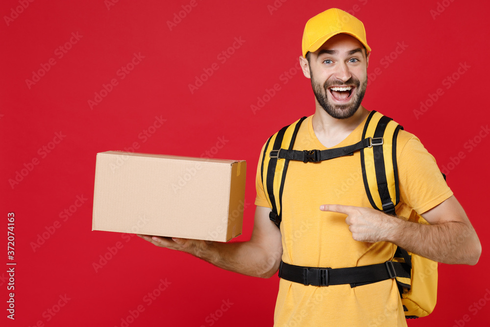 Delivery man in yellow cap t-shirt uniform thermal bag backpack with food hold cardboard box isolated on red background studio Male employee work as courier Service coronavirus covid-19 virus concept Delivery man in yellow cap t-shirt uniform thermal bag backpack with food hold cardboard box isolated on red background studio Male employee work as courier Service coronavirus covid-19 virus concept