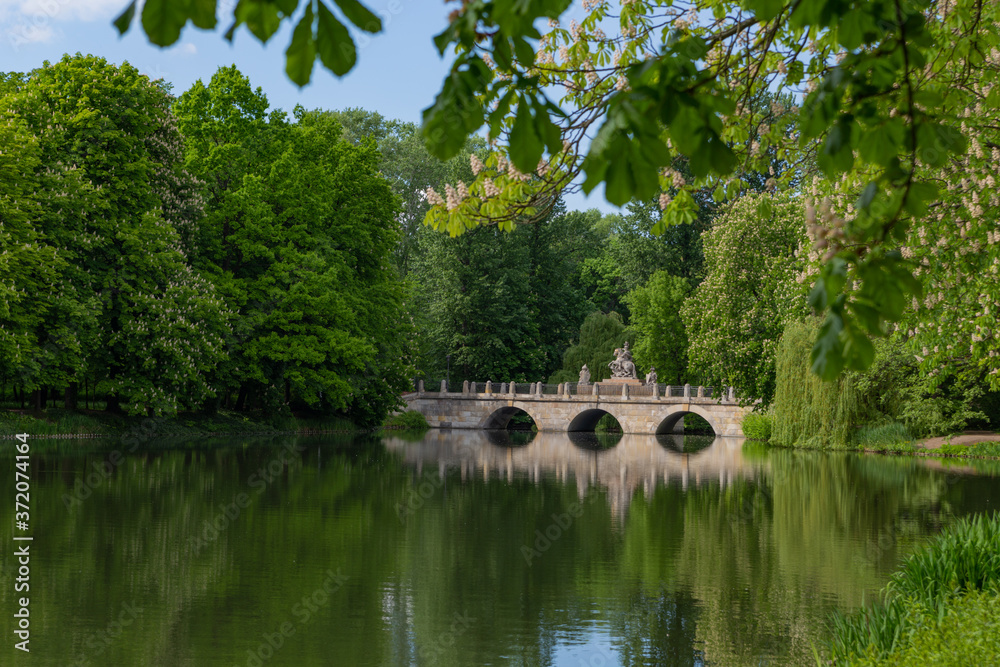 the bridge is reflected in the water across the lake in Royal Baths Park is the largest park in Warsaw, Poland the bridge is reflected in the water across the lake in Royal Baths Park is the largest park in Warsaw, Poland