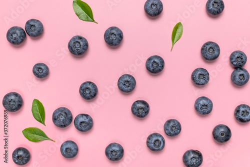 Fresh juicy blueberries with green leaves on pink background. Blueberries background. Flat lay top view copy space. Healthy berry, organic food, antioxidant, vitamin, blue food. Blueberry pattern