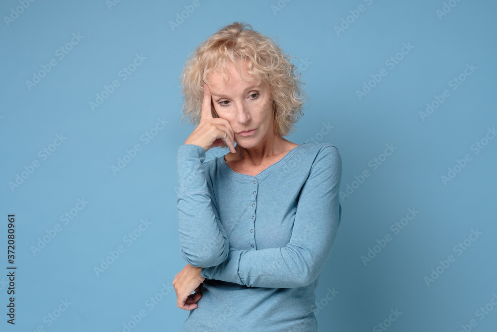 Confused caucasian senior woman thinking making a plan. Studio shot on blue wall.