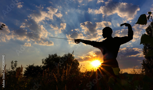 Silhouette of a man with a saber against the background of sunrise or sunset. Freedom fight concept. Outdoor fencing training. photo