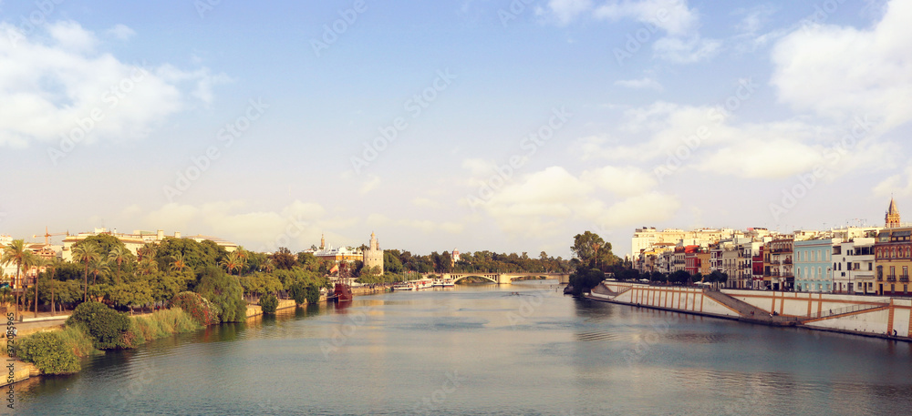 Landscape panorama of Seville with the Guadalquivir river, Triana, the bridge and the city surrounded by palm trees, and a blue sky in the background for a postcard or a wallpaper
