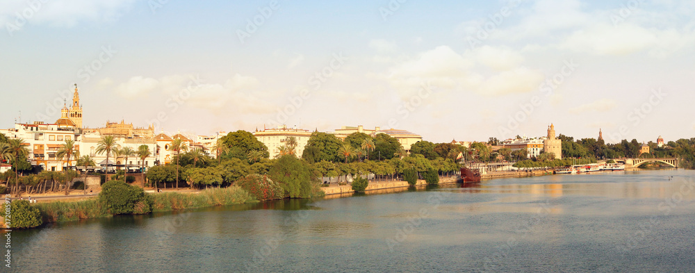 Landscape panorama of Seville coast from Triana, with the Guadalquivir river, the bridge and the monuments of the city, trees and a blue sky in the background for a postcard or a wallpaper