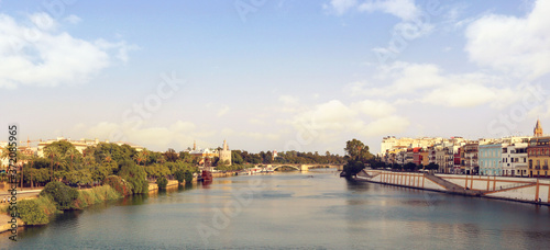 Landscape panorama of Seville with the Guadalquivir river, Triana, the bridge and the city surrounded by palm trees, and a blue sky in the background for a postcard or a wallpaper © Domingo