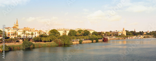 Landscape panorama of Seville coast from Triana, with the Guadalquivir river, the bridge and the monuments of the city, trees and a blue sky in the background for a postcard or a wallpaper