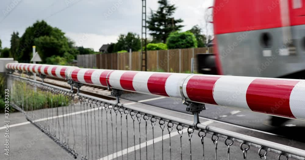 Selected focus view at red and white level crossing railway barrier which block the road until it was lifted, and locomotive move on the rail on countryside in Germany. 