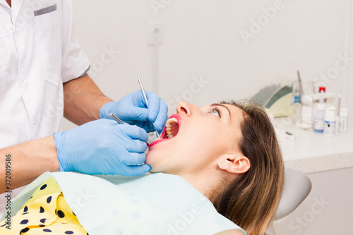 An attractive dark-haired woman, wearing a yellow polka-dot blouse, sits with her mouth open during a teeth whitening procedure. Health concept.