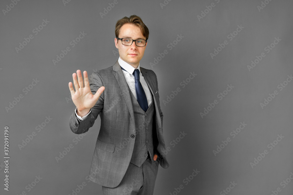 Portrait of a businessman in a suit who stretches out his hand in front of his palm. Stop. Gray background. Portrait of a businessman in a suit who stretches out his hand in front of his palm. Stop. Gray background.