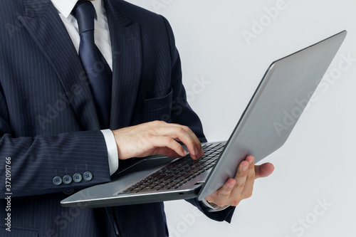 A businessman is holding a laptop in his hands, is typing with one hand. White background. No face visible