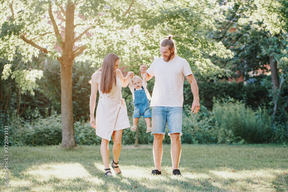 Happy smiling mother and father with baby boy in park outdoors. Family Caucasian mom and dad with son walking hugging in park on summer day. Happy family authentic lifestyle concept. Happy smiling mother and father with baby boy in park outdoors. Family Caucasian mom and dad with son walking hugging in park on summer day. Happy family authentic lifestyle concept.