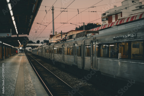 View of a suburban railway platform on a late evening with two railroad tracks: one is empty and there is a modern high-speed train arrived on another track; shallow depth of field, Lisbon, Portugal