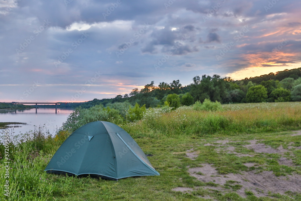 tourist tent on the high bank of the river at sunset