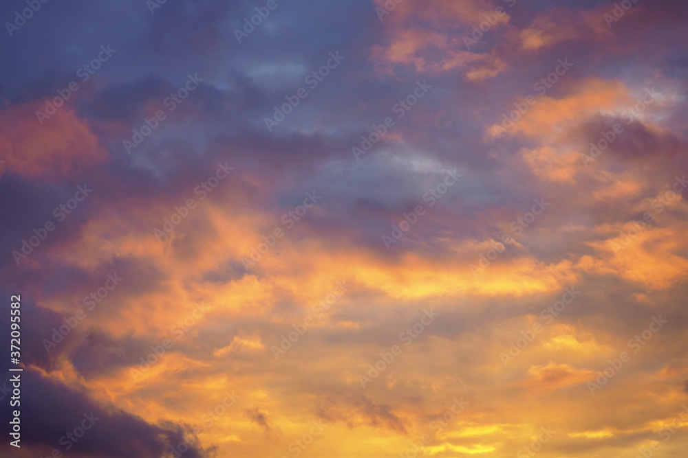 Cloudy sky at sunset. Dark purple-yellow natural background or wallpaper. The rays of the setting sun effectively illuminate the clouds. Beautiful and dramatic evening skies