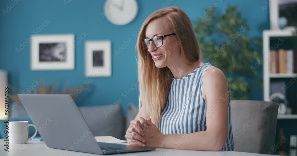 Business lady sitting at table and having working meeting through video chat on laptop. Mature blonde using internet connection for online conversation at home. Business lady sitting at table and having working meeting through video chat on laptop. Mature blonde using internet connection for online conversation at home.