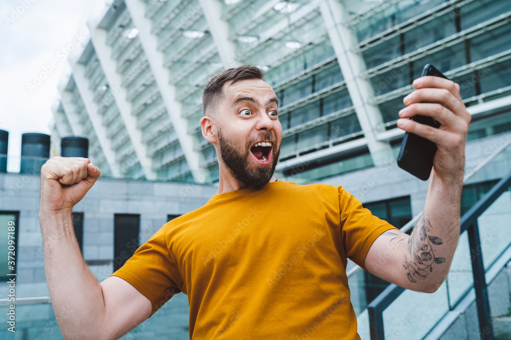 Guy being happy winning a bet in online sport gambling application on his mobile phone Guy being happy winning a bet in online sport gambling application on his mobile phone