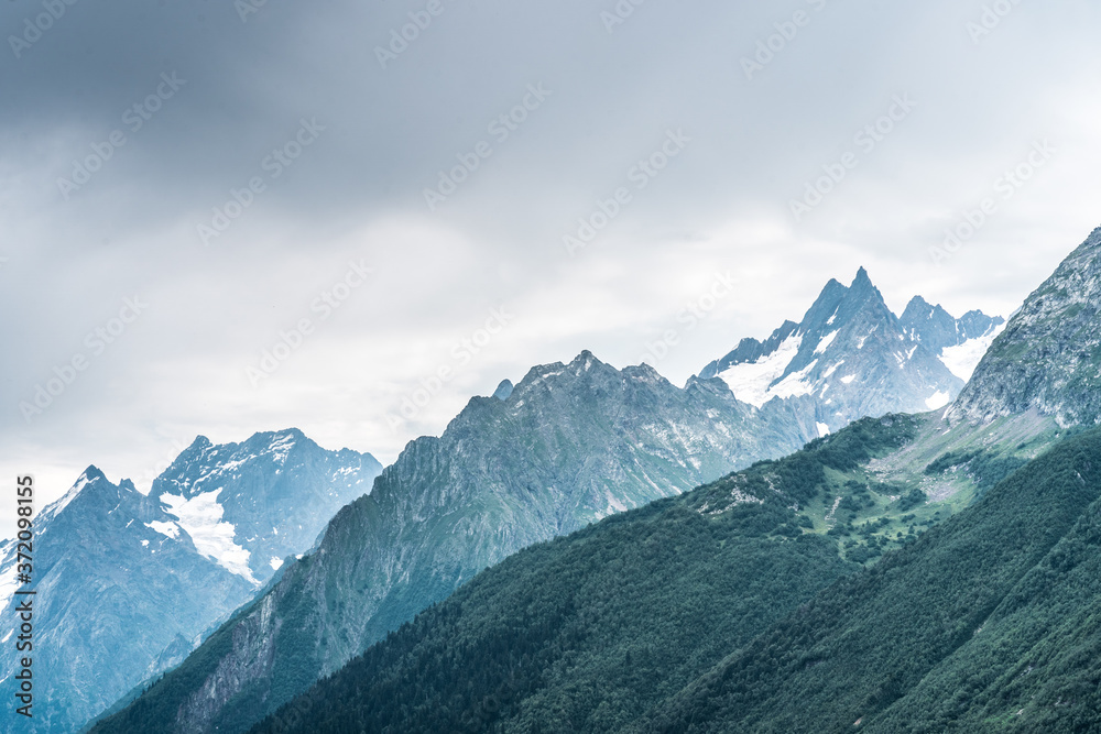 Beautiful mountain landscape in summertime. Mighty mountains with snow in cloudy weather.