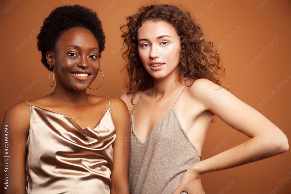 two pretty girls african and caucasian blond posing cheerful together on brown background, ethnicity diverse lifestyle people concept two pretty girls african and caucasian blond posing cheerful together on brown background, ethnicity diverse lifestyle people concept
