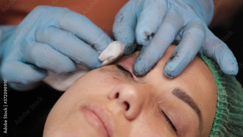 beautician is using small cotton swab for remove dye from eyelids of female client in a beauty salon. beautician is using small cotton swab for remove dye from eyelids of female client in a beauty salon.