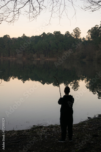 man fishing with a tree branch in a lake in the forest at dusk