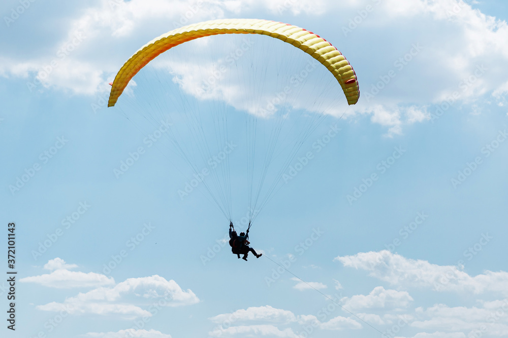 Yellow Paraglider tandem instructor with a tourist flying into the sky with clouds on a sunny day Yellow Paraglider tandem instructor with a tourist flying into the sky with clouds on a sunny day