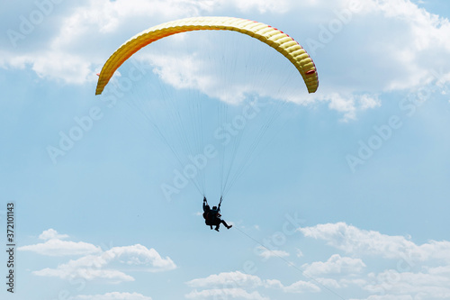 Yellow Paraglider tandem instructor with a tourist flying into the sky with clouds on a sunny day