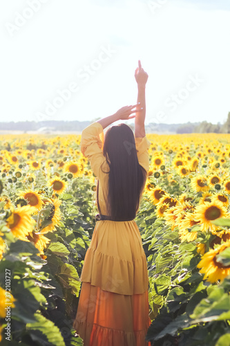 A brunette woman in a yellow dress on the field with sunflowers. Orange dress.