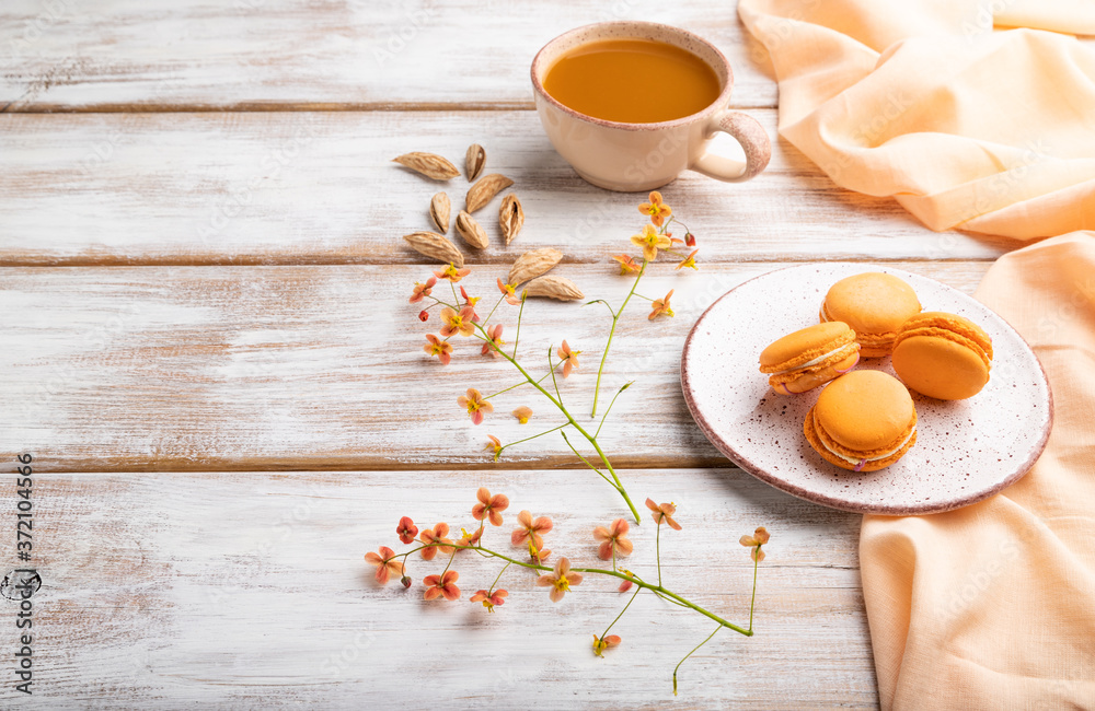 Orange macarons or macaroons cakes with cup of apricot juice on a white wooden background. Side view, copy space. Orange macarons or macaroons cakes with cup of apricot juice on a white wooden background. Side view, copy space.
