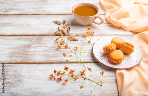 Orange macarons or macaroons cakes with cup of apricot juice on a white wooden background. Side view, copy space.