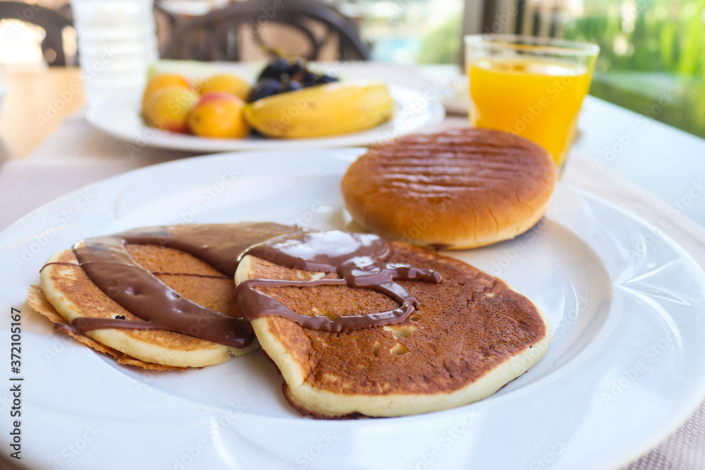 Continental breakfast with pancakes and chocolate served in restaurant. Fruits and orange juice. Morning, outdoor breakfast. Selective focus, close-up