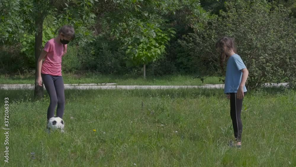 Play with ball in quarantine. Little girls in protective masks play football in the meadow. Children in karate in protective masks. Play with ball in quarantine. Little girls in protective masks play football in the meadow. Children in karate in protective masks.