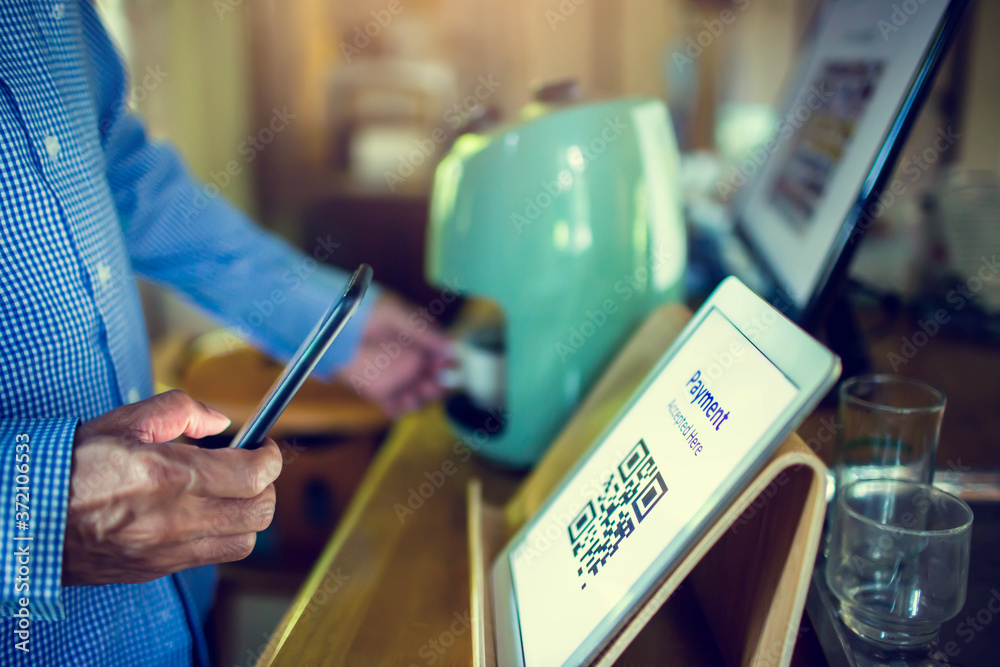 Selective focus to customer using smart phone scan QR code on tablet to payment at counter bar in coffee shop. Accepted generate digital pay without money.