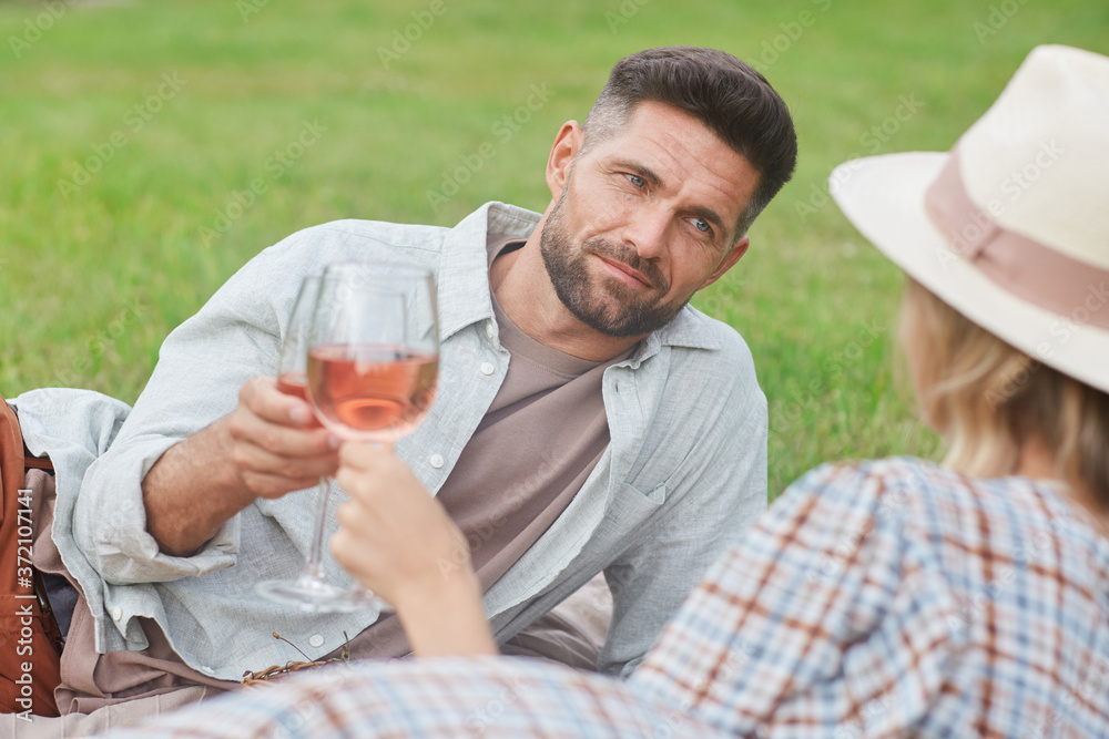 Portrait of handsome mature man holding wineglass while enjoying picnic on green grass during romantic date outdoors Portrait of handsome mature man holding wineglass while enjoying picnic on green grass during romantic date outdoors