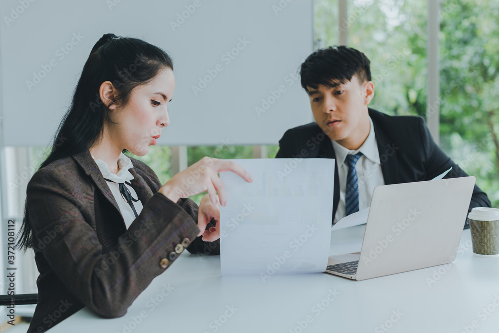 Asian male and female colleagues are discussing work with graph paper and a notebook. Asian male and female colleagues are discussing work with graph paper and a notebook.