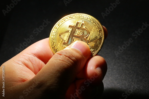 黒い背景のなかで輝くビットコインを掴む手