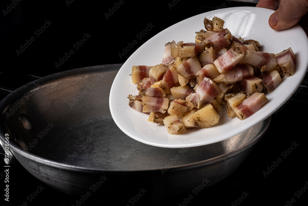 Preparing Spaghetti Carbonara on a black stove with pork guanciale on a white plate on an aluminum pan Preparing Spaghetti Carbonara on a black stove with pork guanciale on a white plate on an aluminum pan