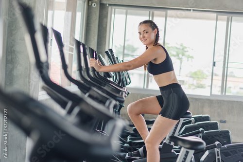 Athlete, woman, girl exercising, biking in the gym. She wears sports clothes to exercise.