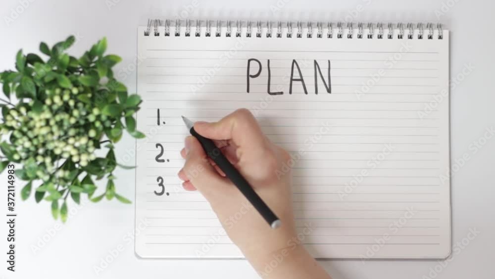Female hand writes in notepad of plan on white background, top view Female hand writes in notepad of plan on white background, top view