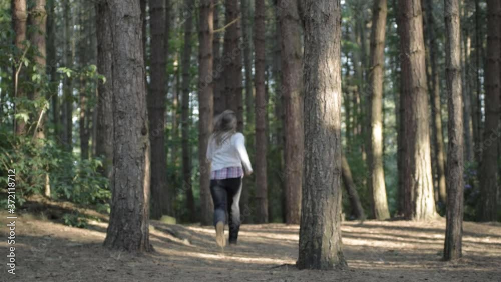 Woman running in empty pine forest with walking stick wide shot