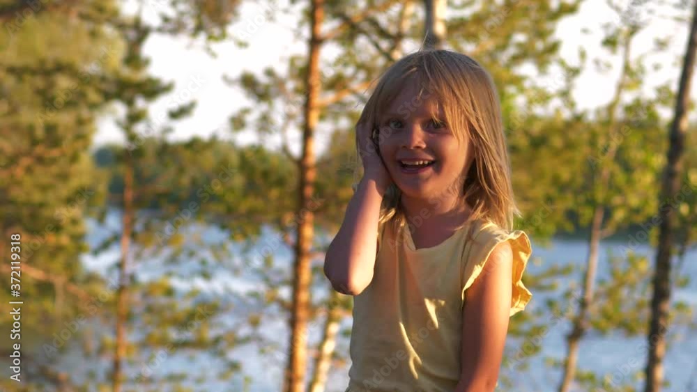 A young blonde girl happily jump and laugh, lake background at sunset A young blonde girl happily jump and laugh, lake background at sunset