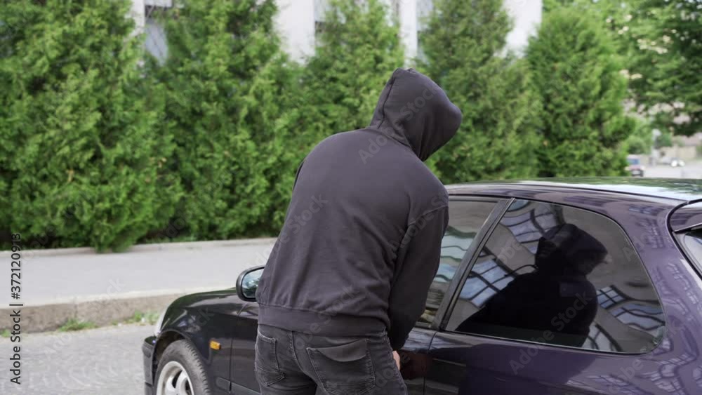Car jacking thief steal car breaking door criminal job burglar Hijacks Auto thief black balaclava hoodie trying break into vehicle screwdriver Street crime violence gangster robber automobile parking Car jacking thief steal car breaking door criminal job burglar Hijacks Auto thief black balaclava hoodie trying break into vehicle screwdriver Street crime violence gangster robber automobile parking