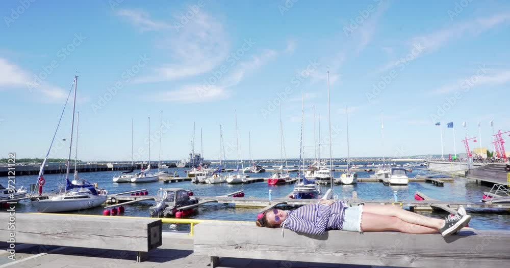 Girl lying on bench yachts harbour and blue sky background