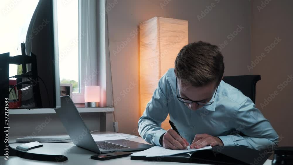 A caucasian businessman working from home with the computer and taking notes on paper A caucasian businessman working from home with the computer and taking notes on paper