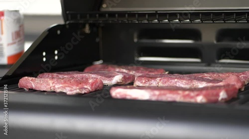 Raw steaks on griddle of matt black outdoor grill, slow motion