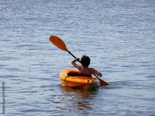 a small boy rowing alone and sitting in an orange kayak