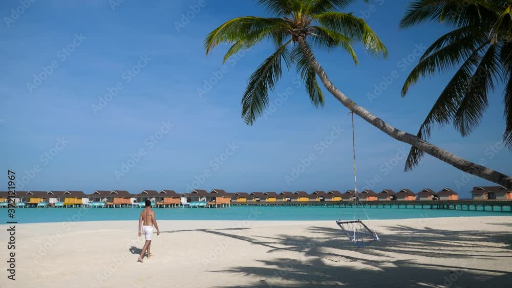 Man walking out alone on prestine white sand beach with palm trees and villas Man walking out alone on prestine white sand beach with palm trees and villas
