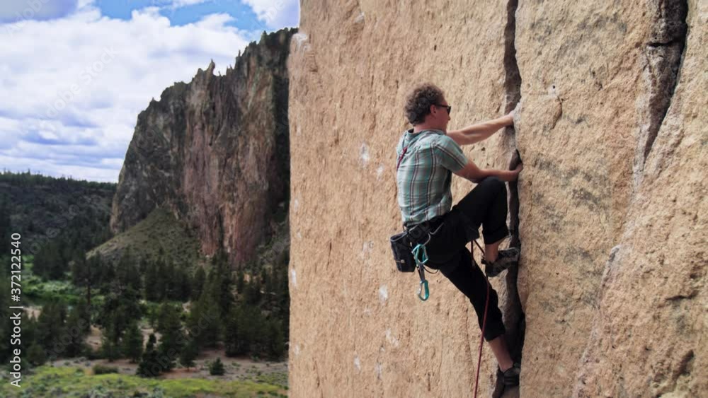 Young male climbing vertical Smith Rock wall locking hands in crack Young male climbing vertical Smith Rock wall locking hands in crack