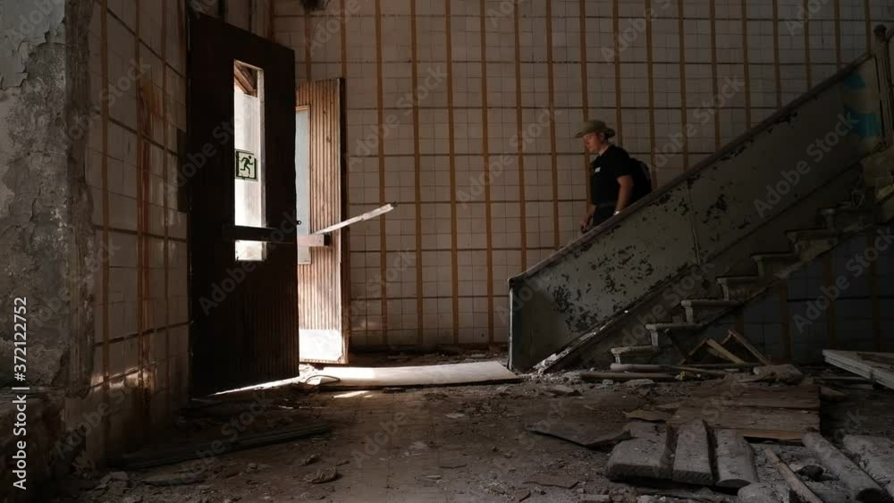 young researcher of European nationality in a hat walks down a dangerous ladder in an abandoned building of an old Soviet factory, goes outside through a door young researcher of European nationality in a hat walks down a dangerous ladder in an abandoned building of an old Soviet factory, goes outside through a door