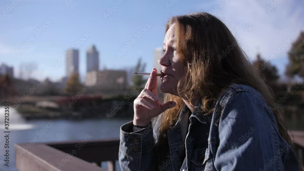 Tired, homeless woman taking a drag on her cigarette. Part of a series in slow motion where she smokes. Tired, homeless woman taking a drag on her cigarette. Part of a series in slow motion where she smokes.